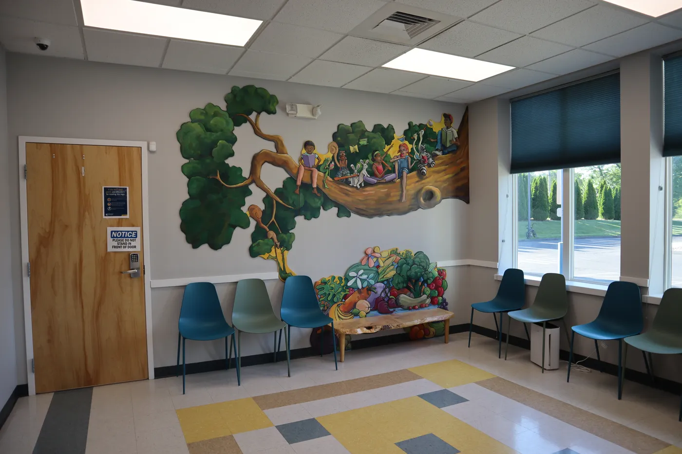 A waiting room at The Pediatric Care Center with a painted tree mural of children reading